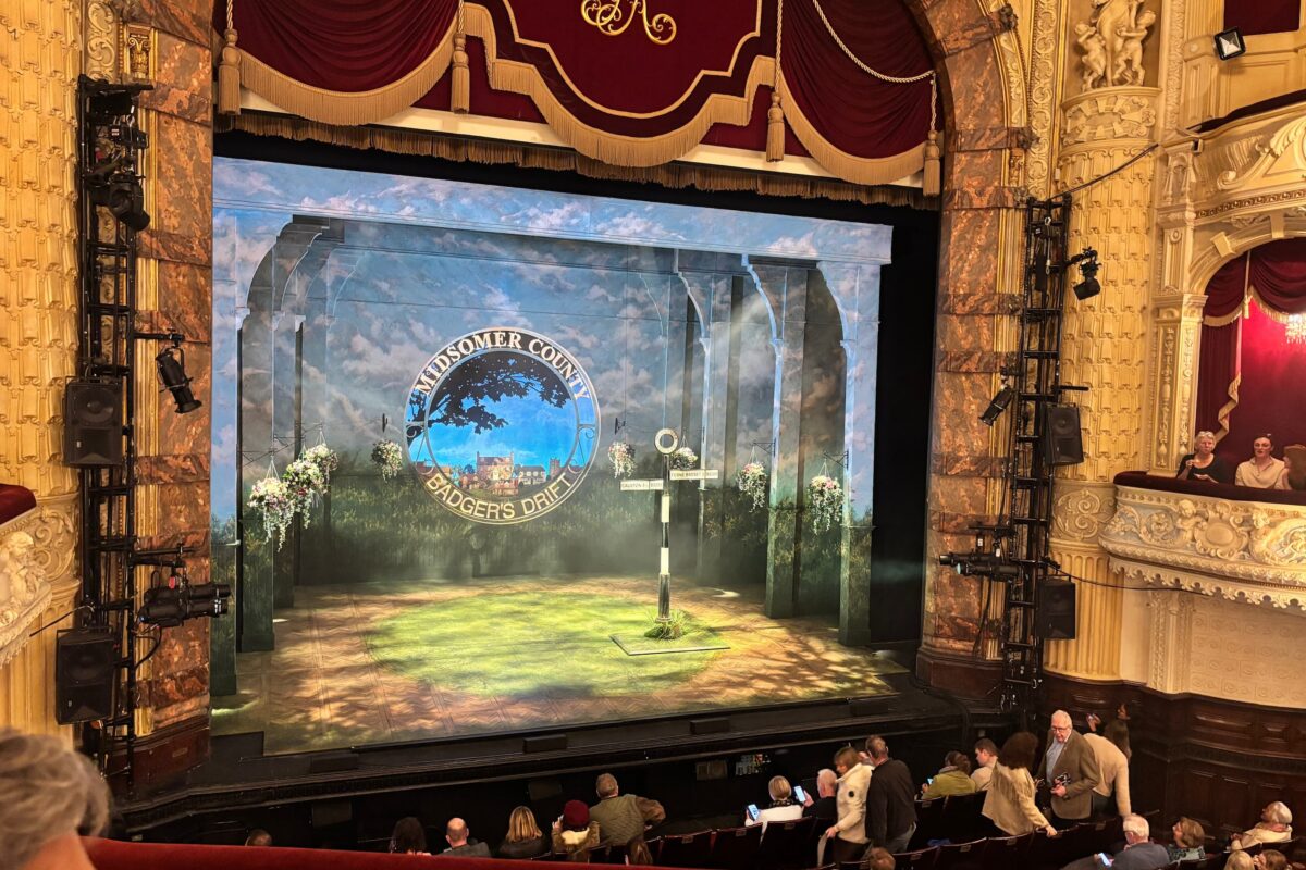 Stage view of Midsomer Murders: The Killings at Badger’s Drift at Richmond Theatre, showing the Badger’s Drift village sign and part of the audience before the performance.