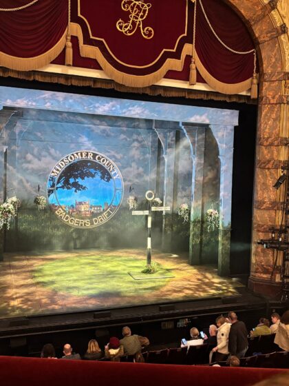 Stage view of Midsomer Murders: The Killings at Badger’s Drift at Richmond Theatre, showing the Badger’s Drift village sign and part of the audience before the performance.