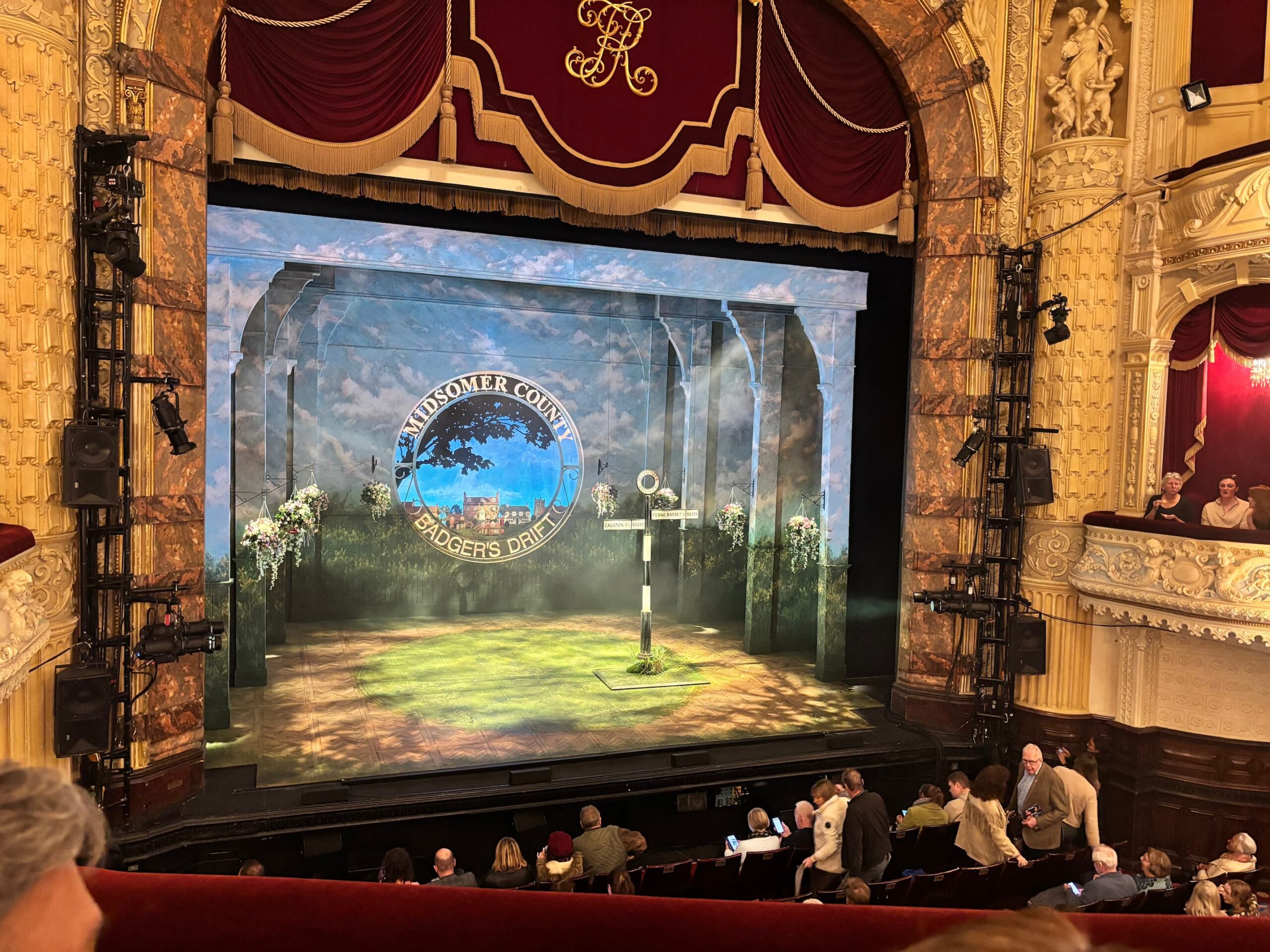 Stage view of Midsomer Murders: The Killings at Badger’s Drift at Richmond Theatre, showing the Badger’s Drift village sign and part of the audience before the performance.